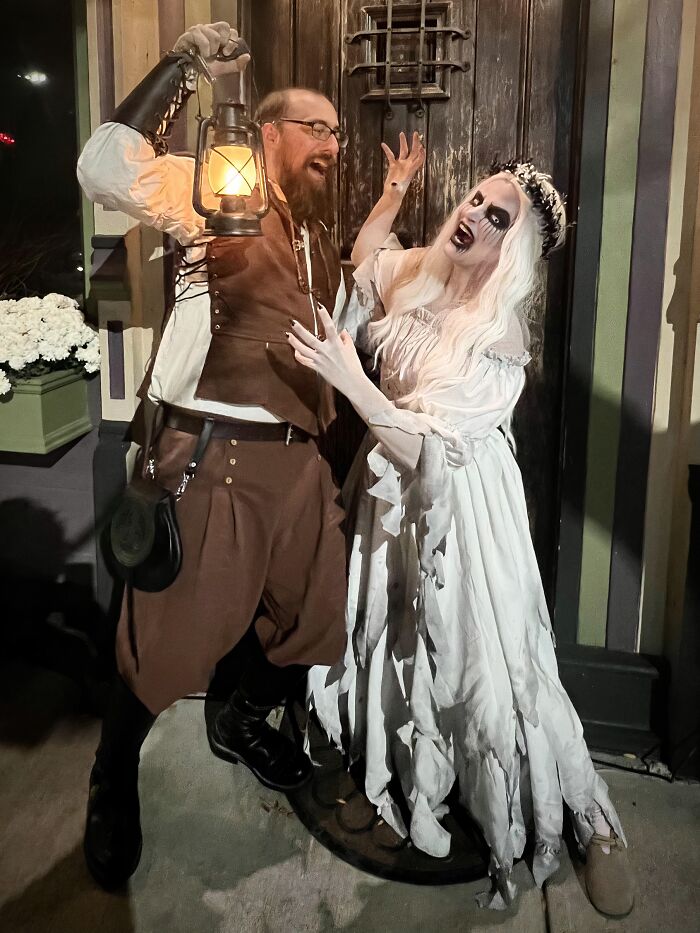 A man with a lantern and a ghastly woman dressed in a ghost bride outfit for Halloween couples costumes.