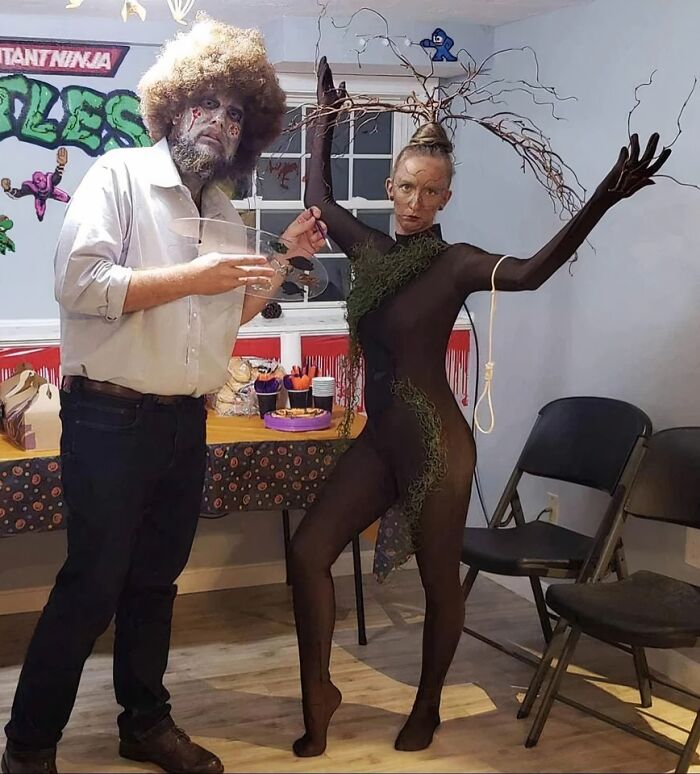 A man and woman wearing funny Halloween couples costumes dressed as Bob Ross and a happy little tree