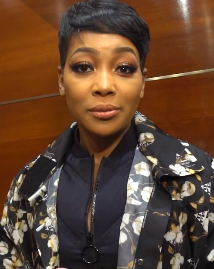 Singer Monica posing with a stylish short pixie haircut and floral jacket reflecting her career highlights