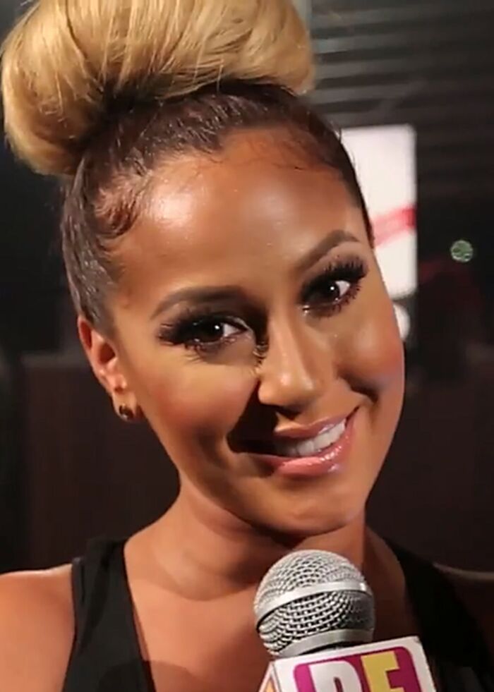 Close up of Adrienne Bailon smiling while holding a microphone at an event