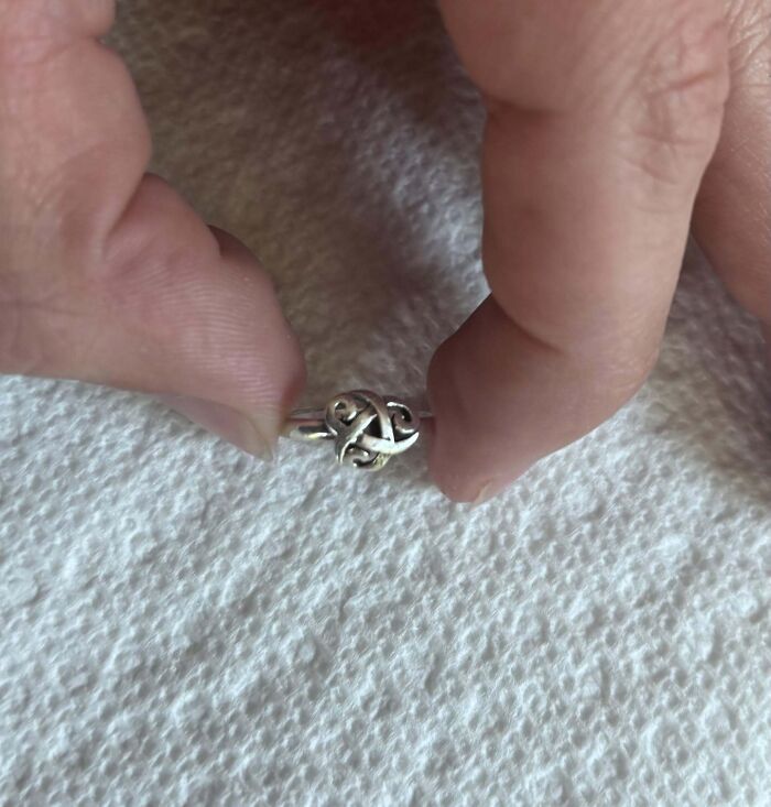 A hand holding a small, intricate silver ring, reminiscent of real-life photos with a horror movie feel.