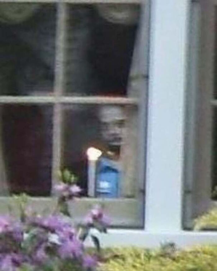 Creepy face peering out from a window behind a candle, looking like a real-life horror movie image