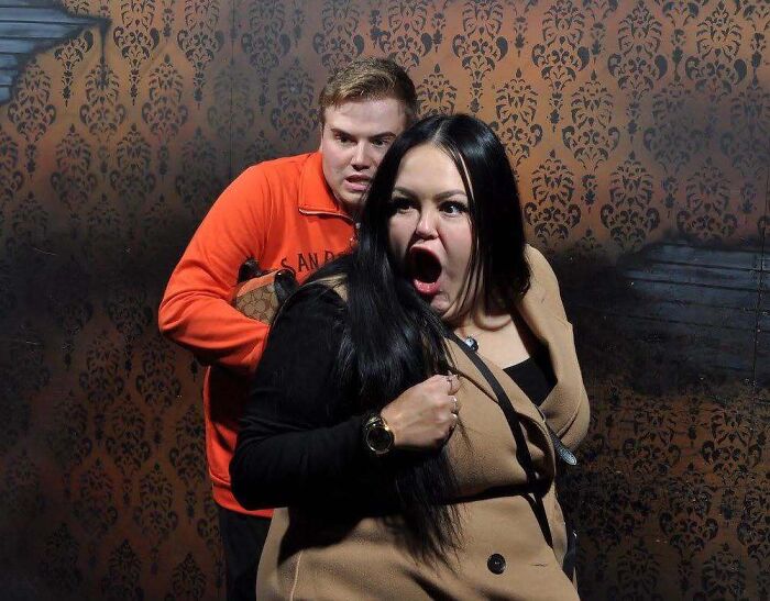 Woman screaming in fear next to a man in orange in haunted house photos.