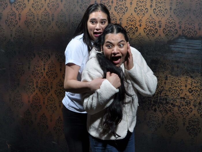 Two women look terrified and scream while clinging together in haunted house photos.