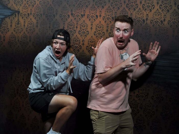 Two terrified young men flinch with open mouths in haunted house photos.