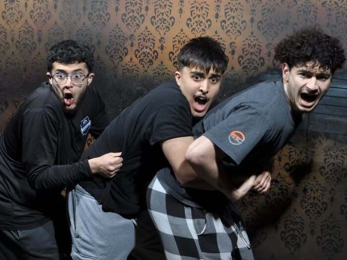 Three young men with shocked faces hold onto each other in haunted house photos.