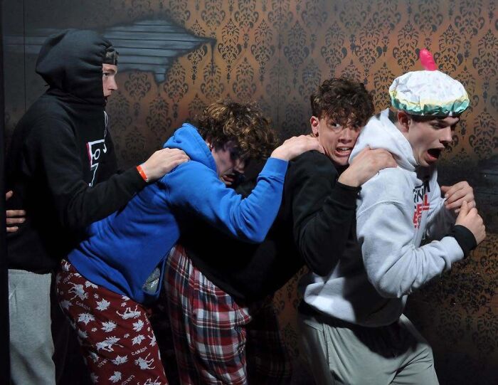 A group of scared young men cower together in a funny haunted house photo.