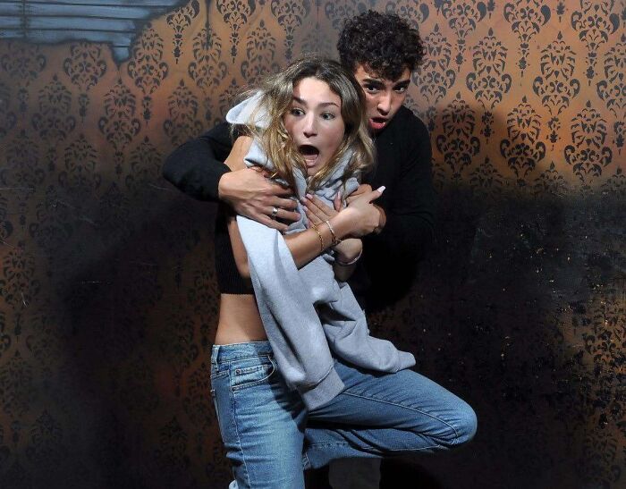 A terrified young couple reacts with shock inside a spooky haunted house photo setup.