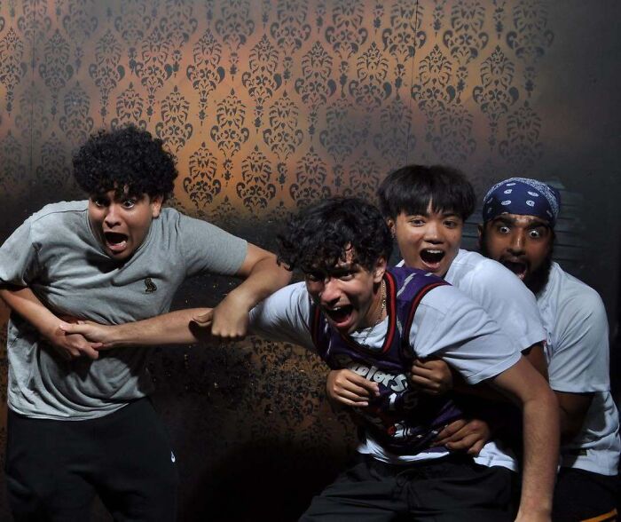 Four young men clinging to each other in fear in candid haunted house photos taken at a jump scare.