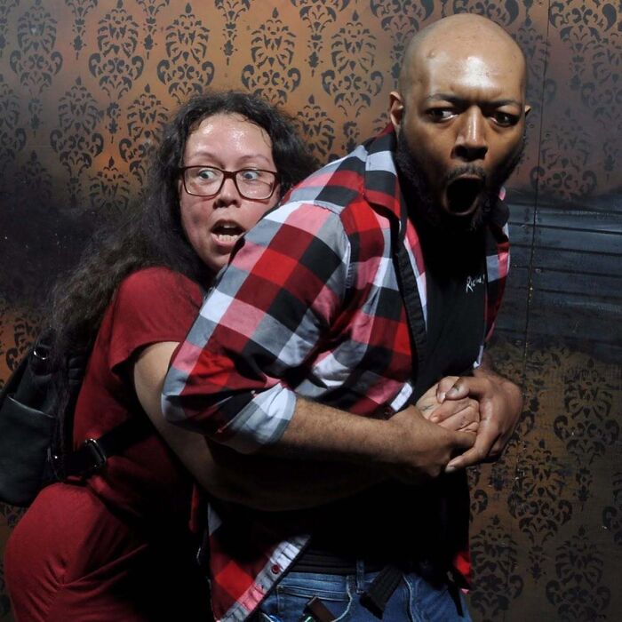 Panicked couple screaming in pure terror in a funny haunted house photo taken inside a dark room.