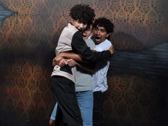 Three young men hugging tightly in fear for a haunted house photo.