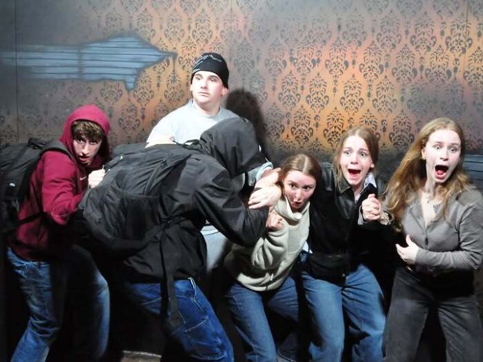 A group of friends cower and scream in terror during a haunted house jump scare.