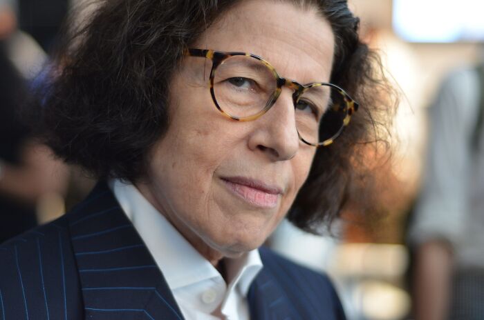 Close-up portrait of author Fran Lebowitz wearing tortoise-shell glasses and a suit jacket