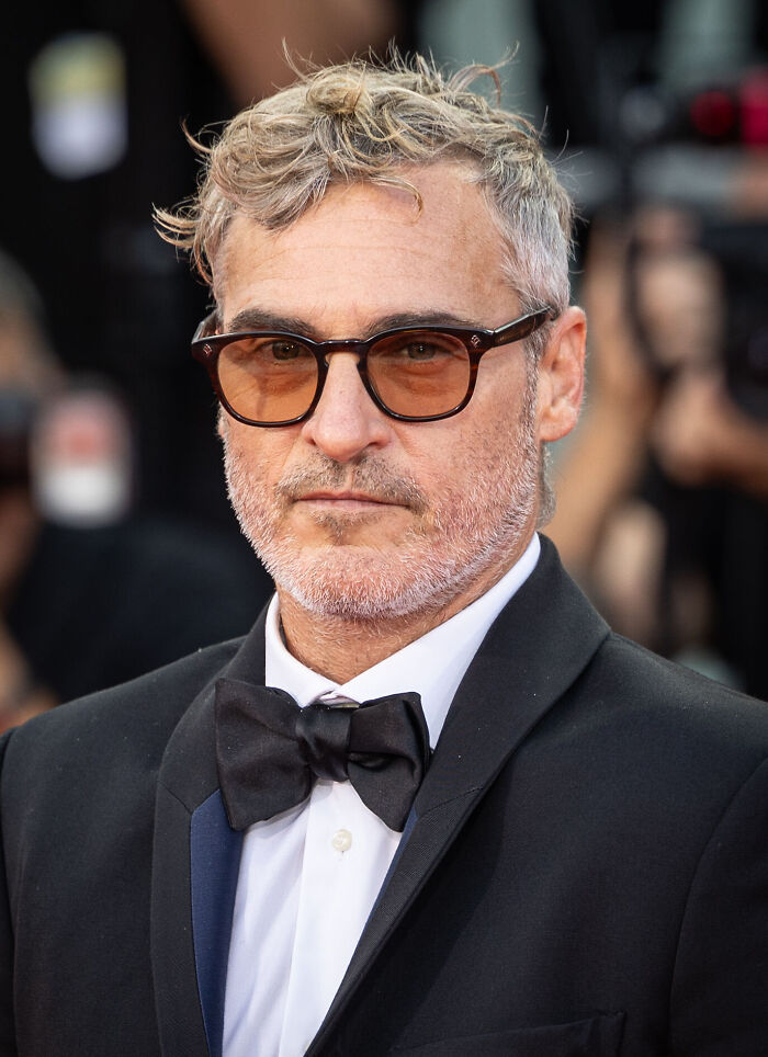 Actor Joaquin Phoenix wearing tinted glasses and a tuxedo with a black bow tie at a red carpet event