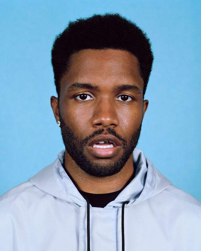 Close-up portrait of Frank Ocean in a light jacket against a blue backdrop highlighting his career highlights