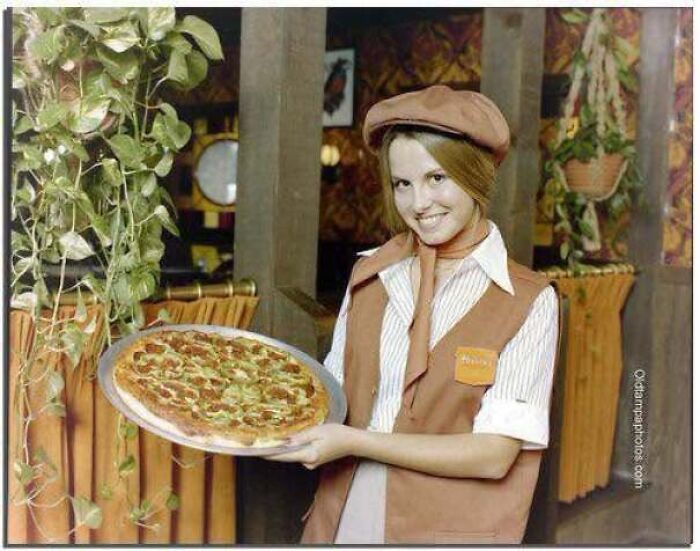 A 1970s waitress holding a freshly baked pizza, featured in old photos of America.