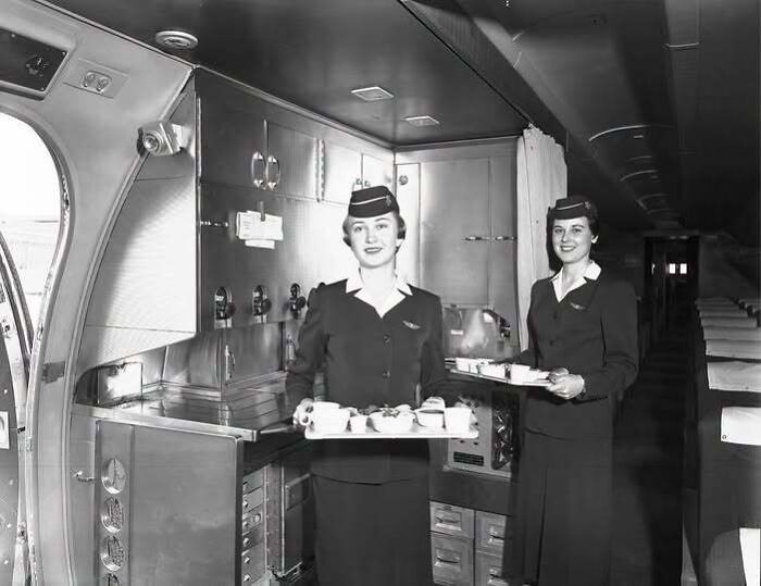 Black and white old photo of flight attendants preparing food in an airplane kitchen in America