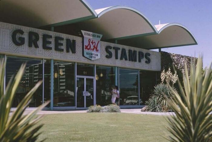 An old photo of America featuring a S&H Green Stamps redemption center building on a sunny day.