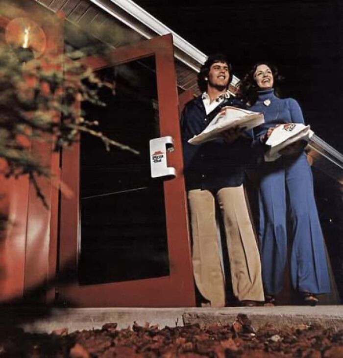 A happy young couple leaving a Pizza Hut restaurant in an old photo of America.