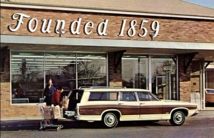 An old photo of America showing a classic station wagon parked in front of a store established in 1859.