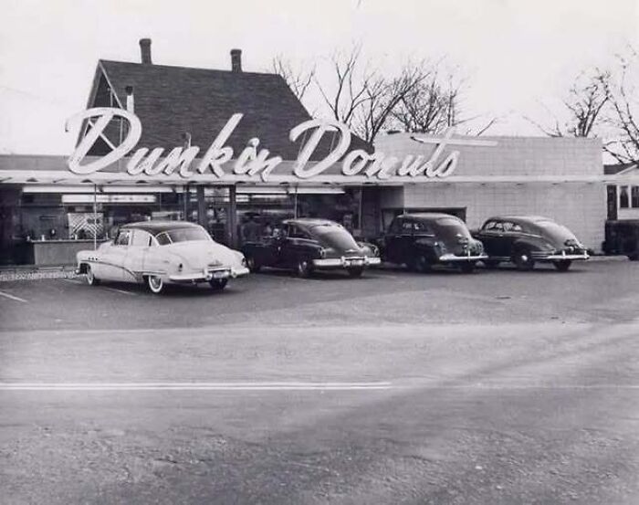 Black and white vintage picture showcasing classic cars parked outside an early Dunkin Donuts storefront