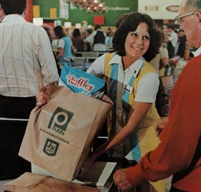 A friendly supermarket cashier packing groceries in a paper bag, showcasing old photos of America style nostalgia.