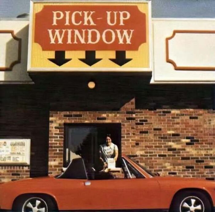 An orange classic car at a fast food drive-thru pick-up window captured in old photos of America.