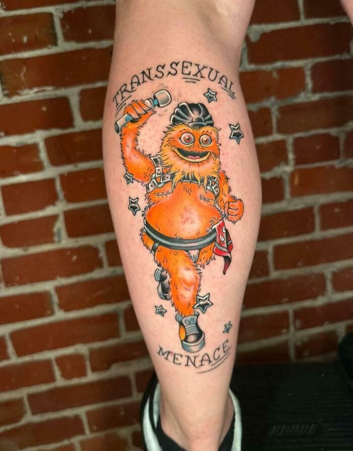 A tattoo of Gritty wearing leather gear with Transsexual Menace text, part of well-made creations.