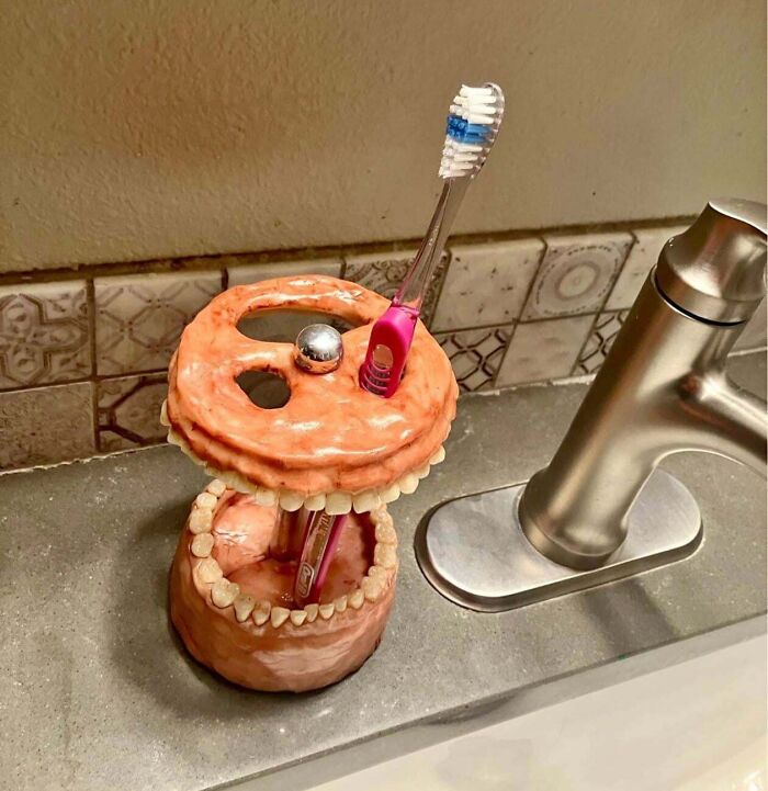 An awful toothbrush holder creation shaped like realistic gums and teeth next to a sink.