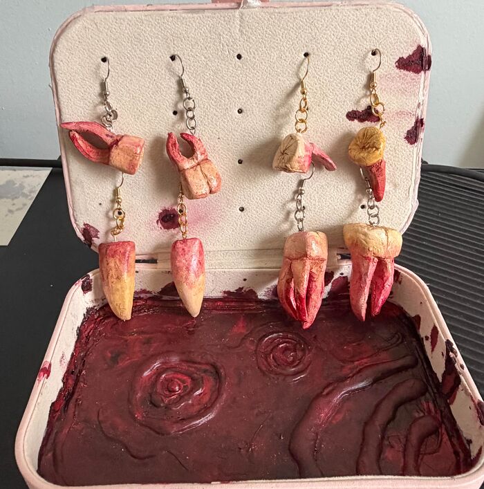 Creepy handcrafted teeth earrings inside a bloody display case showing creations awful to look at.
