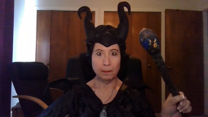 Funny Halloween photo of a woman dressed as Maleficent holding a staff indoors