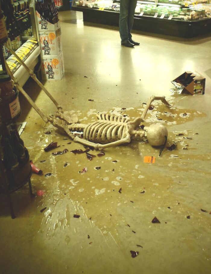 A skeleton lying on a store floor near spilled beer bottles, funny Halloween didn’t go as planned moment