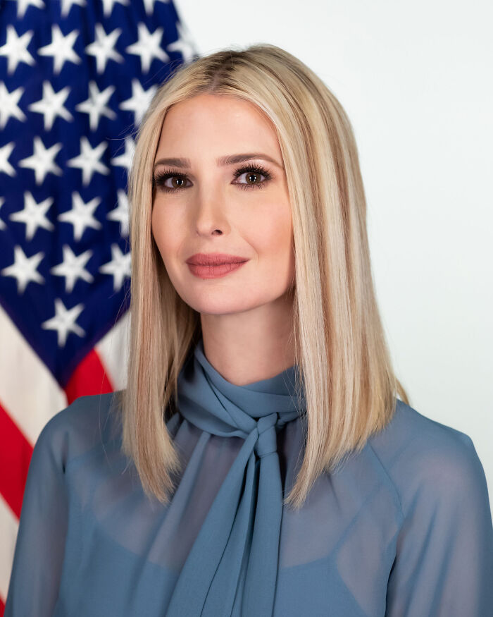 Official portrait of Ivanka Trump wearing a blue top in front of an American flag.