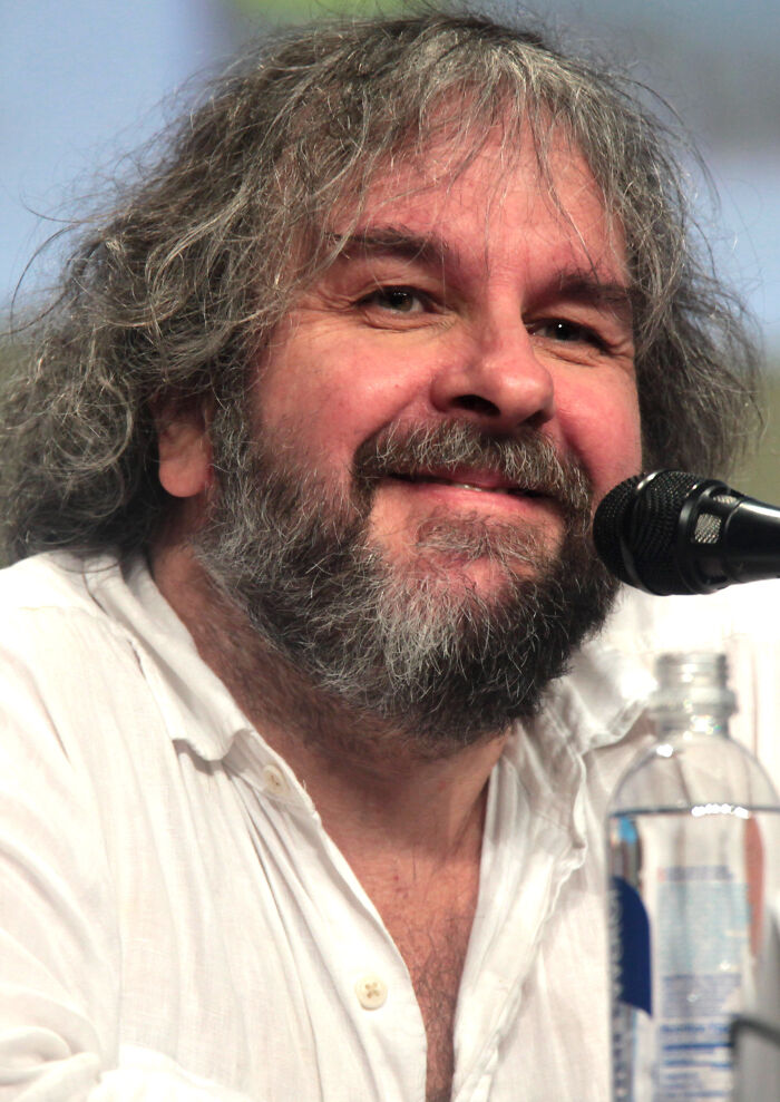 Filmmaker Peter Jackson smiling at a microphone panel speaking about his bio and career highlights.