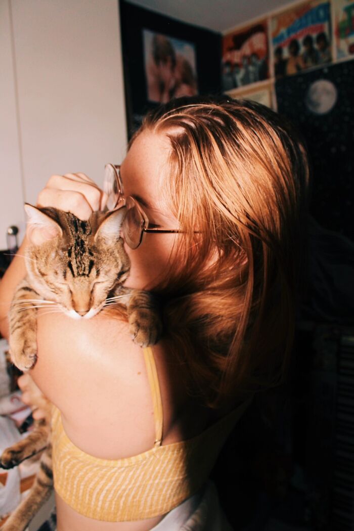 A woman cuddling her sleeping tabby cat close, showcasing life stories shared with pets