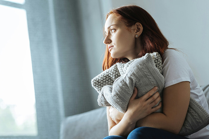 Pensive woman clutching a grey sweater while reflecting on uncovering lies days before her ex's funeral. Pensive woman clutching a grey sweater while reflecting on uncovering lies days before her ex's funeral.