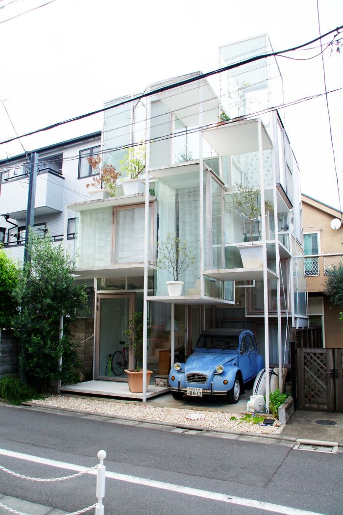 Modern transparent cube house with car parked underneath on narrow city street