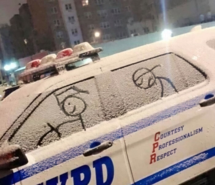 A stick figure driver drawn on a snow-covered police car, showing a lighthearted act of vandalism.