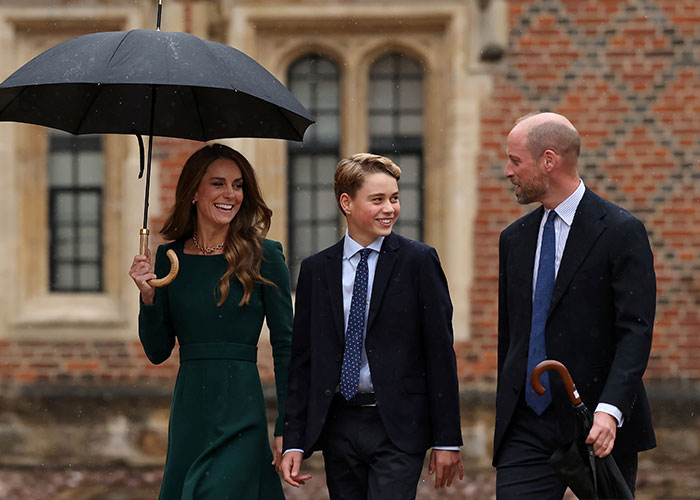 Prince George smiles as he walks beside Kate Middleton and Prince William under a black umbrella. Prince George smiles as he walks beside Kate Middleton and Prince William under a black umbrella.