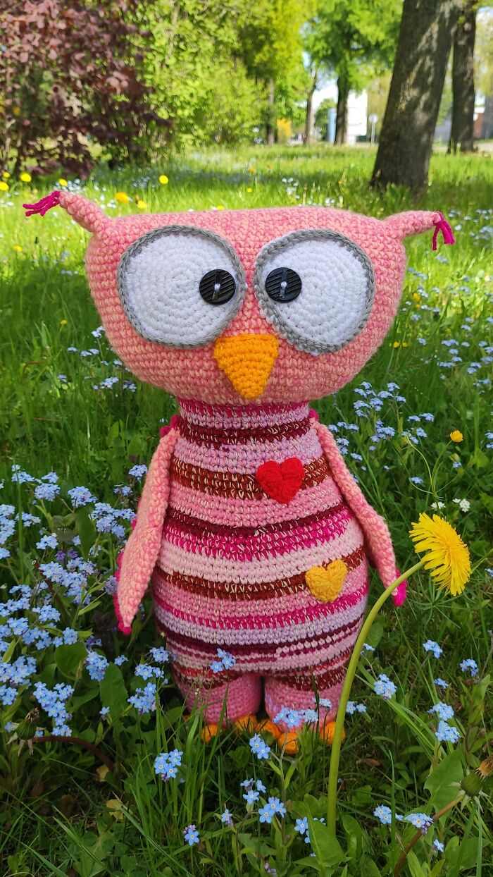 A pink and orange striped owl crochet toy stands in a field of blue wildflowers.
