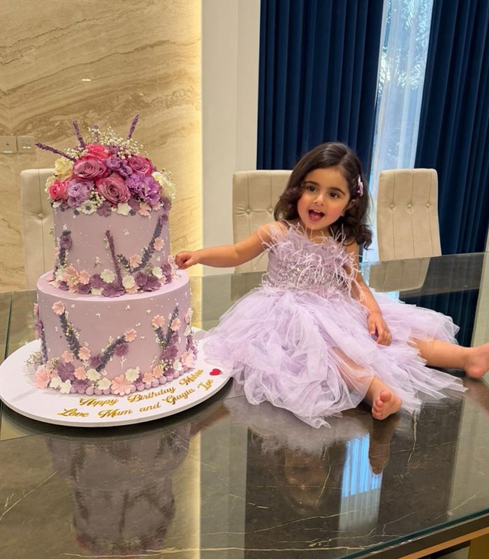 Young child in a lavender dress sitting next to a decorated birthday cake