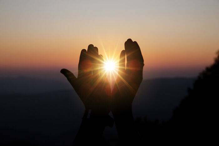 Silhouetted hands raised toward a bright sun flare during a cults ritual.