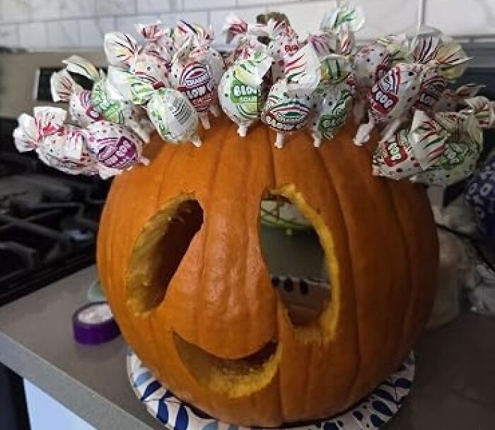 A carved Halloween pumpkin decorated with lollipops sticking out of the top, perfect for Halloween candies lovers