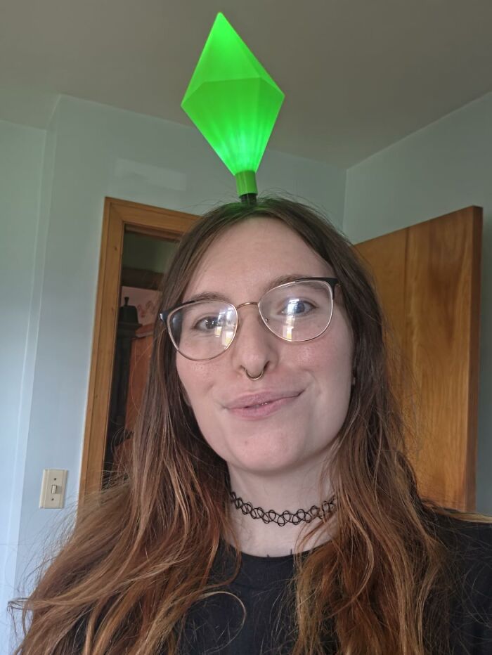 A woman wearing a glowing green Sims plumbob headband as a low-effort Halloween costume.