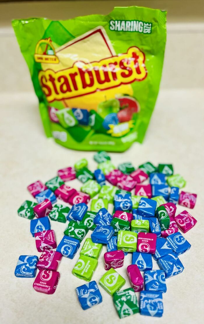 A pile of colorful chewy Starburst candies spilled in front of a green bag for Halloween candies lovers