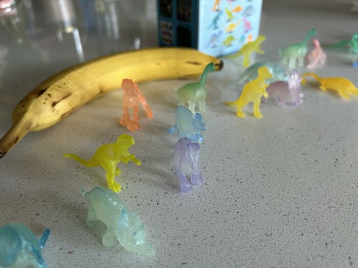 Small colorful translucent dinosaur toys arranged with a banana