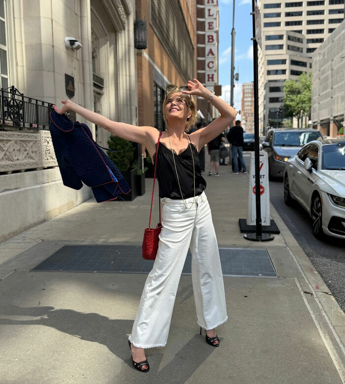 Selma Blair posing enthusiastically on a city sidewalk in wide-leg white pants and a black top. Selma Blair posing enthusiastically on a city sidewalk in wide-leg white pants and a black top.