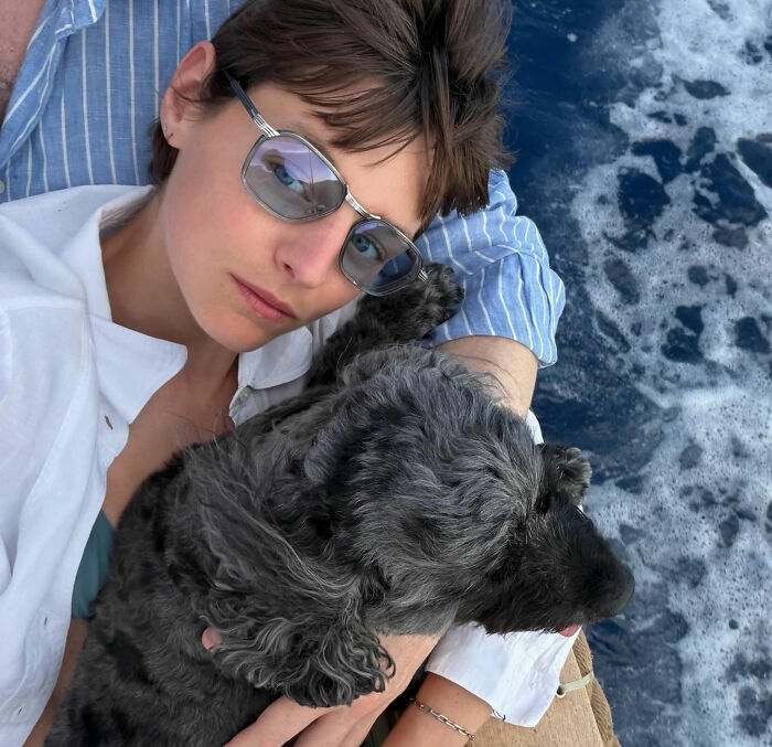 Trans actress wearing sunglasses, sitting with a dog by the sea