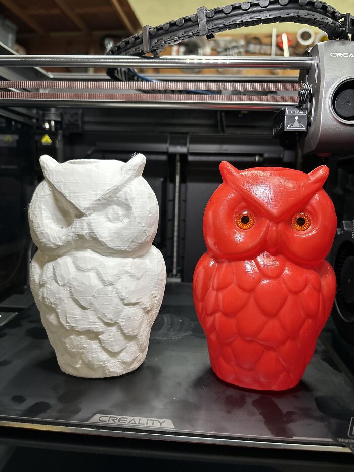 Two owl figurines, one white and one red, showcase detailed 3D prints.