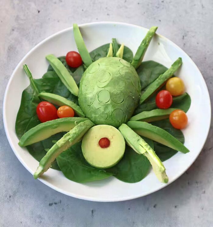 An avocado turtle sculpture arranged on a bed of spinach, demonstrating everyday food turned into playful works of art